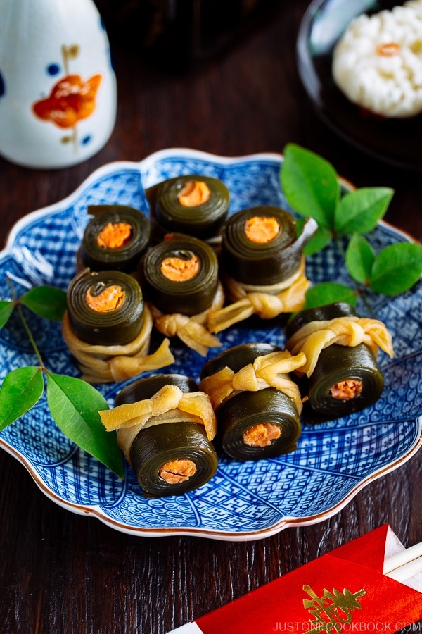 Japanese blue plate containing Salmon Kombu Roll garnished with green leaves.