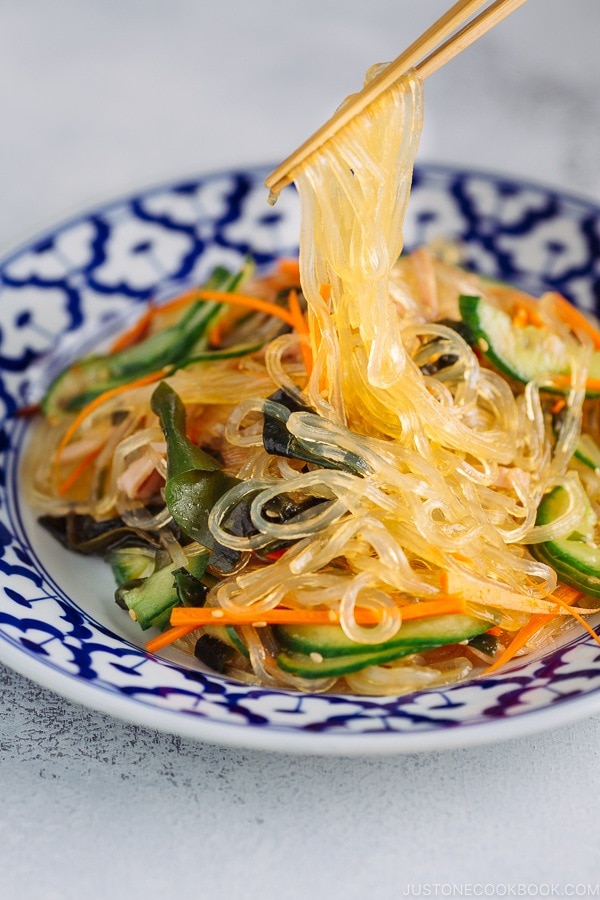 Chopsticks holding glass noodles being pulled out from the delicious Harusame Salad (Japanese Glass Noodle Salad) on a blue and white plate.