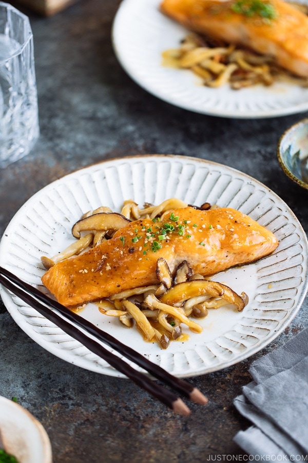 White plate containing Miso Butter Salmon served with sauteed shiitake and shimeji mushrooms.