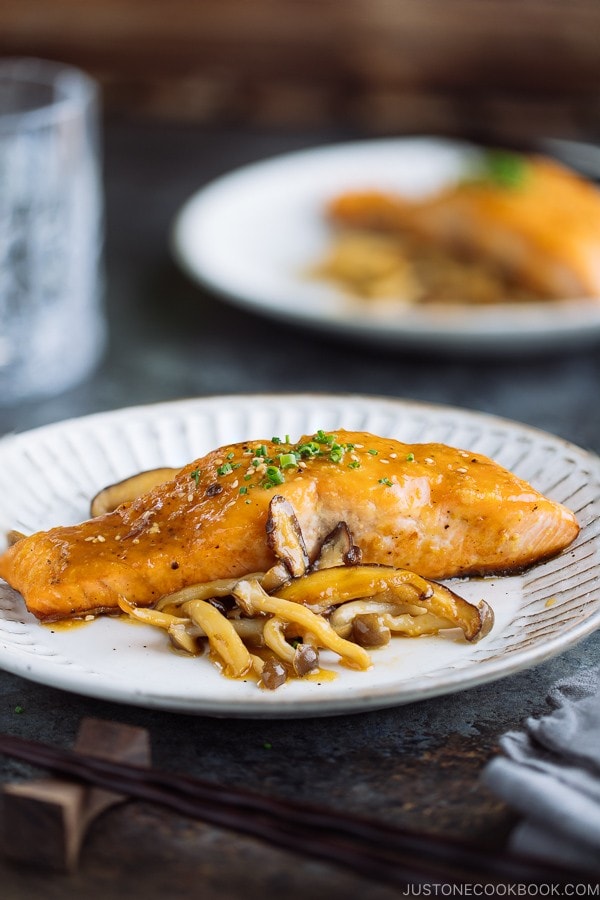 White plate containing Miso Butter Salmon served with sauteed shiitake and shimeji mushrooms.