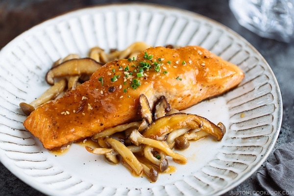 White plate containing Miso Butter Salmon served with sauteed shiitake and shimeji mushrooms.