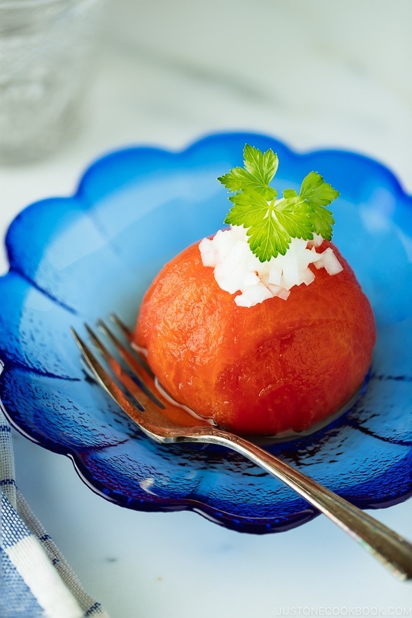 A blue glass containing Japanese-style Pickled Tomatoes garnished with minced onion.