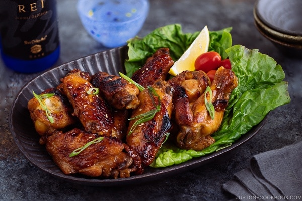 Teriyaki wings served on a dark brown plate garnished with lemon, tomatoes and green lettuce.