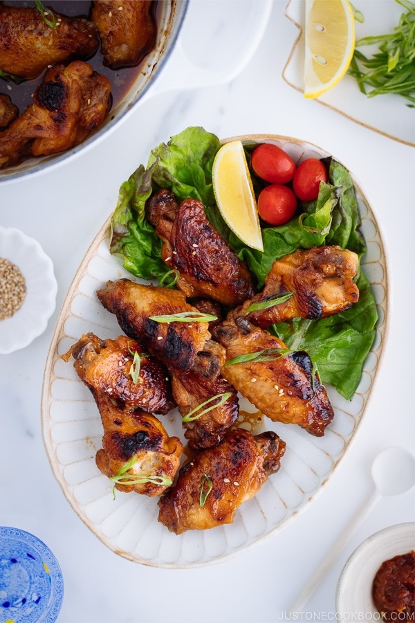 Teriyaki wings served on a white plate garnished with lemon, tomatoes and green lettuce.