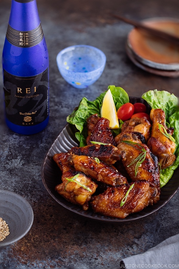 Teriyaki wings served on a dark brown plate garnished with lemon, tomatoes and green lettuce.