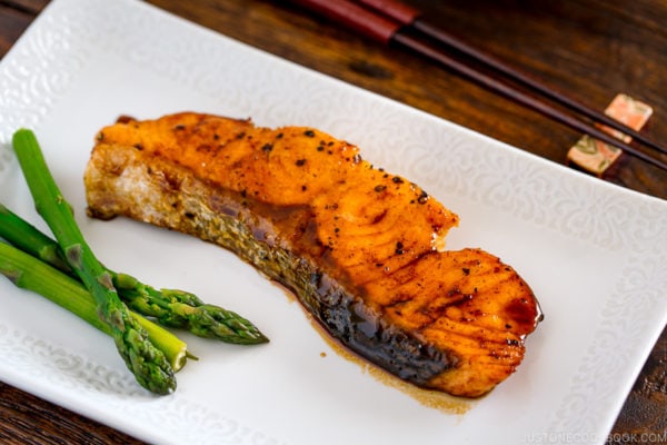 A white plate containing teriyaki salmon with glaze and asparagus.
