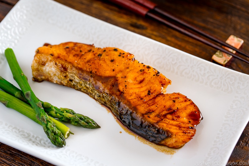 A white dish containing teriyaki salmon with icing and asparagus.