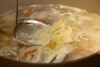 a ladle skimming foam off soup in a pot