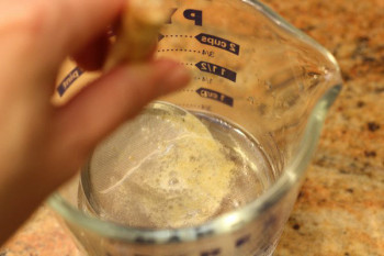 a ladle with scum in a measuring cup with water