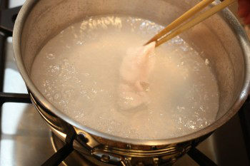 chopsticks holding a thin slice of work cooking pan with hot water