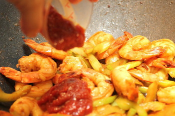 ketchup pouring into shrimp stir fry in a metal pan