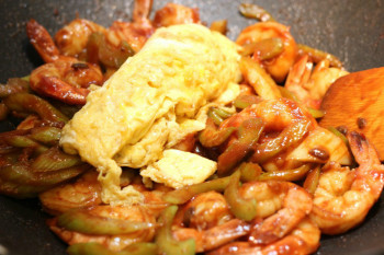 egg poured into shrimp stir fry in a metal pan