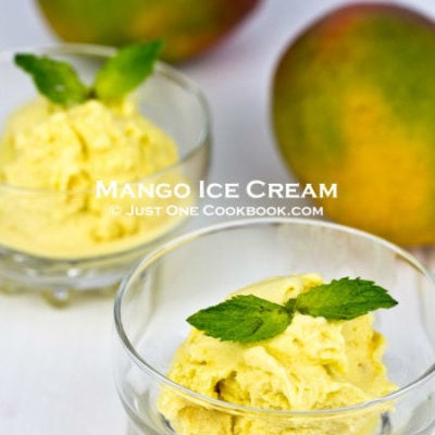 mango ice cream in a glass bowl next to mangos on white board