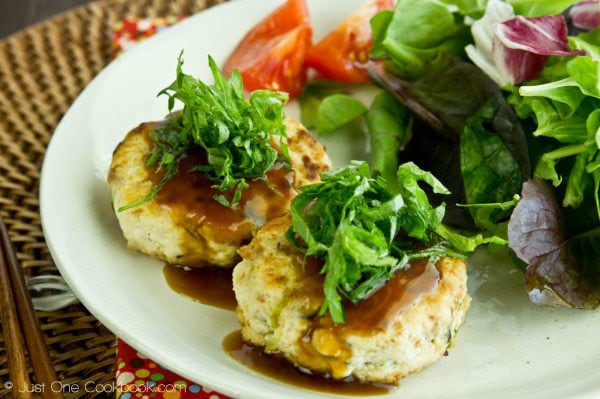 Chicken & Tofu Hamburger Steak topped with shiso and soy glaze and salad on a white plate.