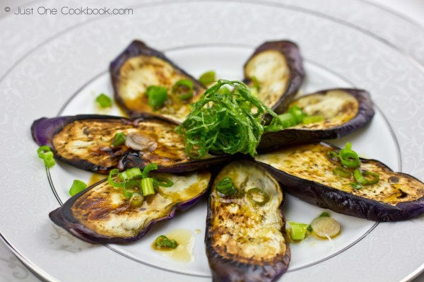 Eggplant with Sesame Ponzu Sauce topped with shiso and green onion on a plate.