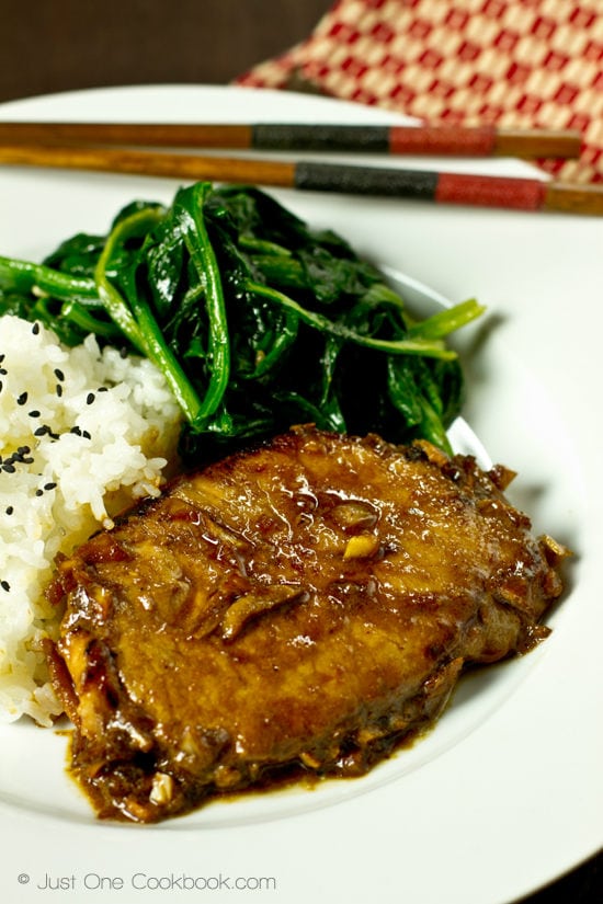 Asian Pork Chop with white rice and sauteed spinach on a white plate.
