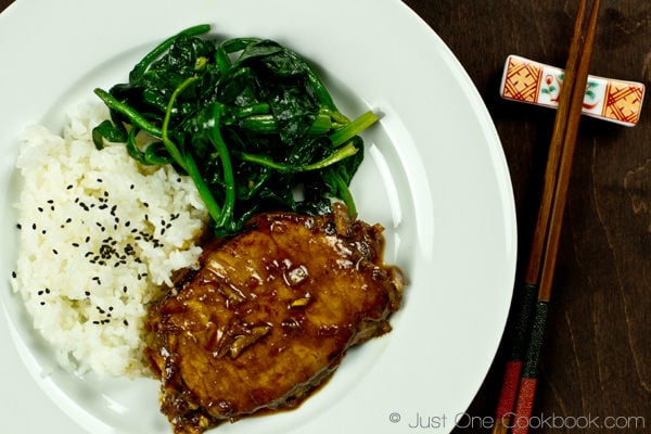 Asian Pork Chop III Asian Pork Chop with white rice and sauteed spinach on a white plate.