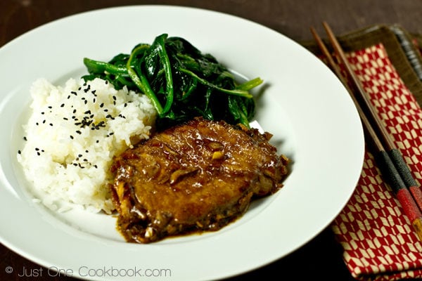 Asian Pork Chop with white rice and sauteed spinach on a white plate.