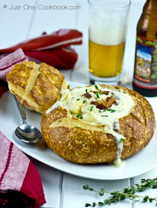 Clam Chowder in a bred bowl on a white plate and a glass of beer on a side.