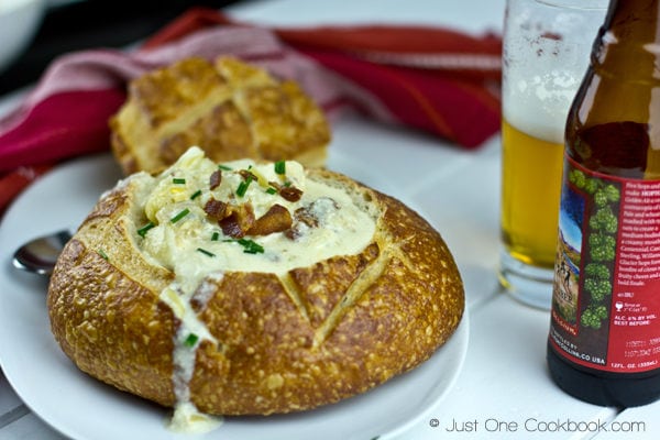 Clam Chowder in a bread bowl and beer on a white table.