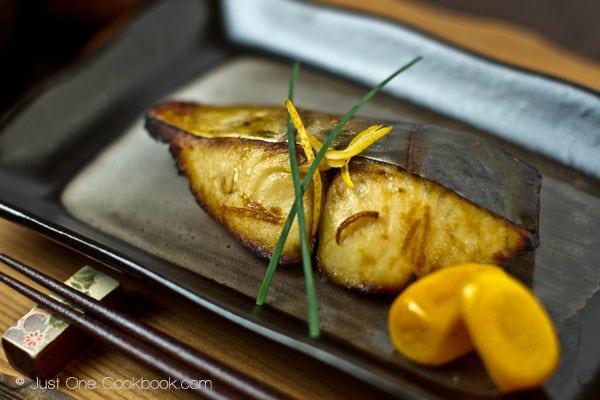 Spanish Mackerel with Yuzu on a black plate.