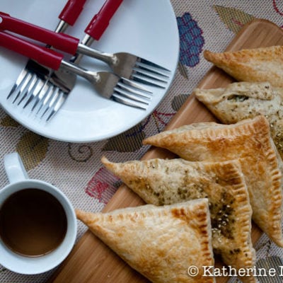 Spinach and Feta Turnovers on a table with plates, forks, and a cup of tea.
