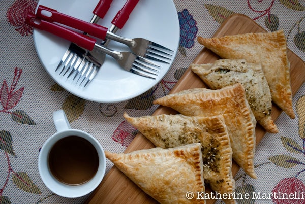 Spinach and Feta Turnovers on a cutting board with a cup of tea, and plates and forks on a table.