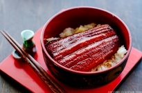 A classic Japanese dish Unadon in a Japanese lacquer bowl containing steamed rice, grilled eel fillet caramelized in sweet soy-based sauce.