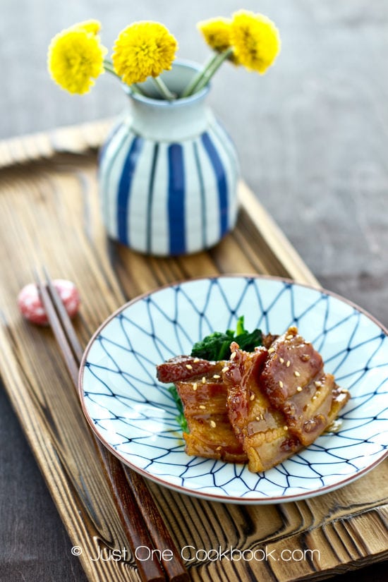 Honey Pork Belly with spinach in a plate and yellow flower in a flower pot.