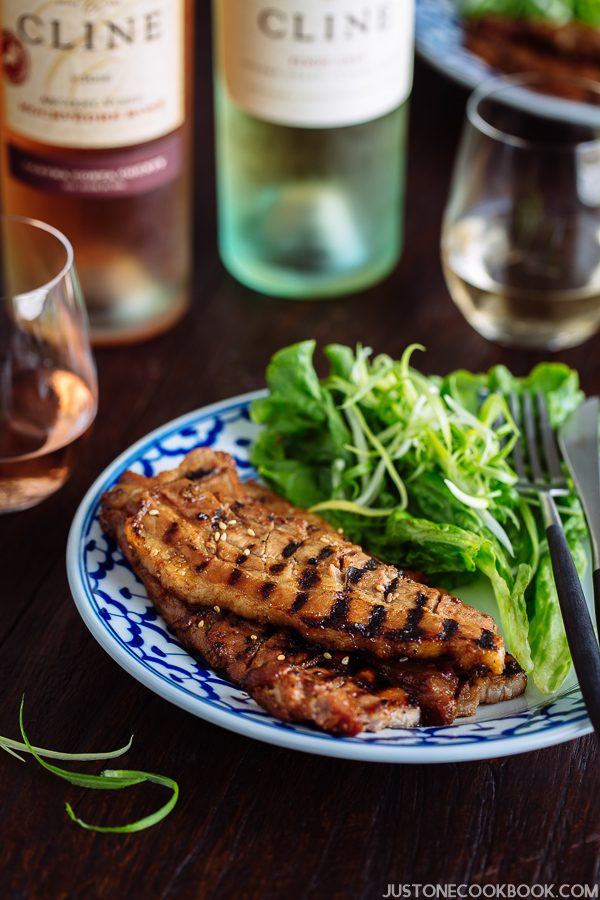 BBQ Pork Belly with salads on the plate and bottle of wine on the wooden table.