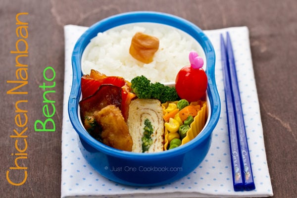 Chicken nanban bento box with chicken nanban, tamagoyaki, mixed vegetable, and umeboshi on a table.
