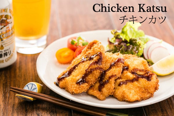 Chicken Katsu with salad on a plate and a glass of beer on a wooden table.