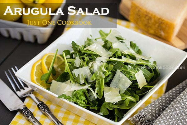 Arugula Salad with shaved Parmesan cheese in a white dish.