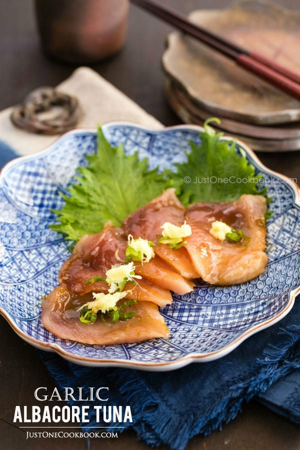 Garlic Albacore Tuna sashimi topped with scallion and ginger on a plate.