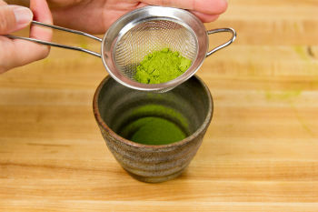 green tea in a strainer on top of a tea cup on cutting board