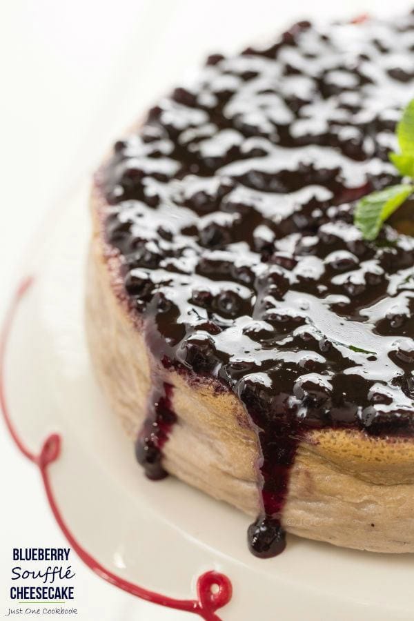 Blueberry Soufflé Cheesecake topped with blueberry jam on a cake stand.