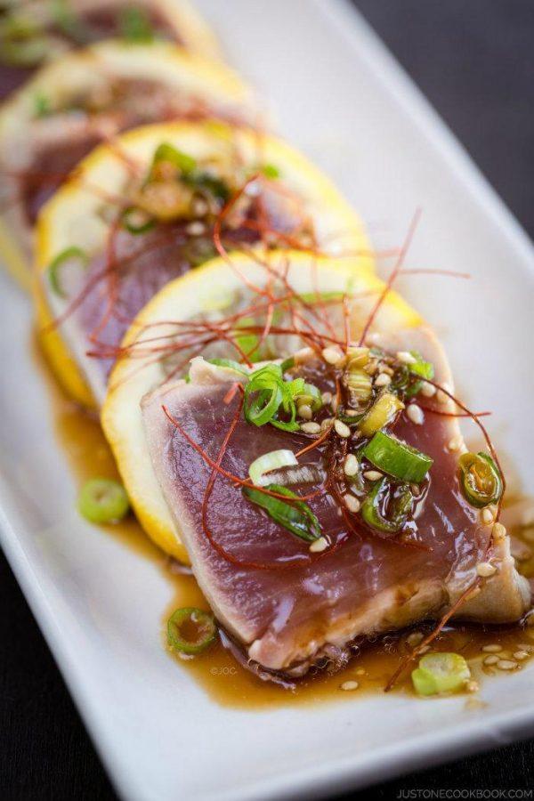 Tuna Tataki and sliced lemons on a white plate.