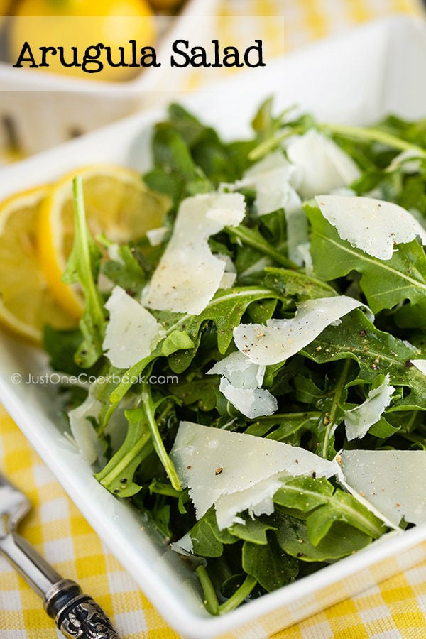 Arugula Salad with shaved Parmesan cheese in a white dish.