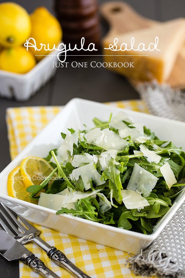 Arugula Salad with shaved Parmesan cheese in white dish.