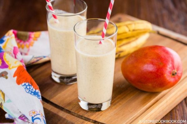 Two glasses of Mango Coconut Smoothie, mango and banana on a table.