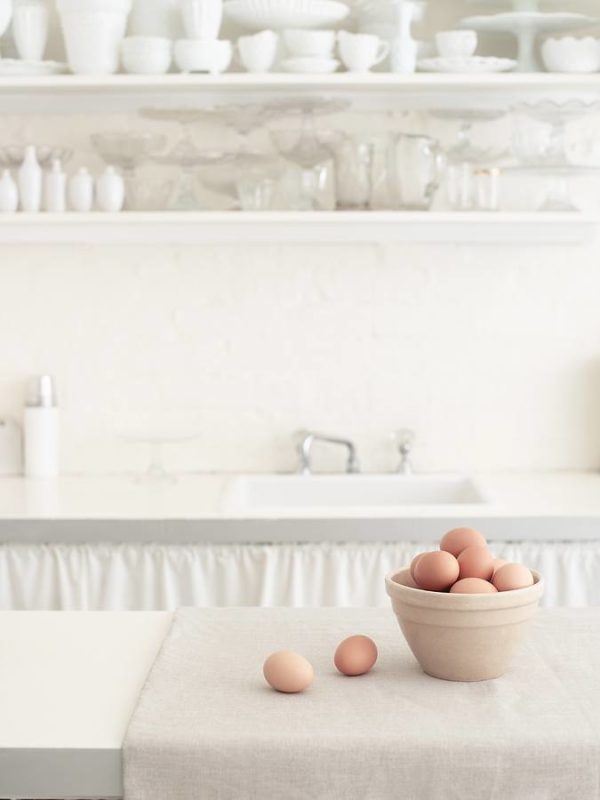 Basket of brown eggs on countertop with bowls on shelf in white
