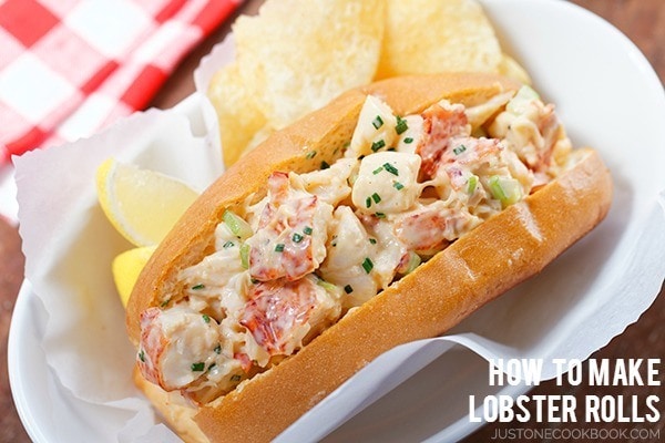 Sweet, succulent lobster meat coated with spicy mayo is piled into a buttery toasted bun and chips on a plate.
