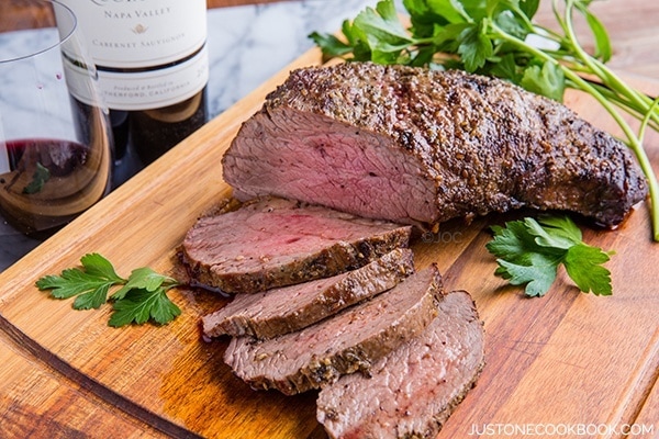 Tender and Juicy Wood-Smoked Tri-Tip on a cutting board and wine on a table.