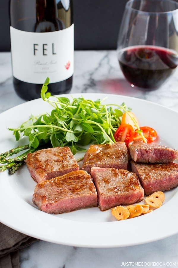 Wagyu beef steak and salad on a white plate and a bottle and glass of wine.