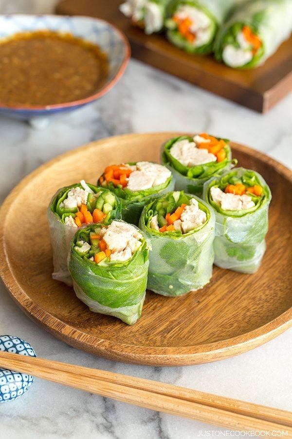 Chicken Spring Rolls on a wooden plate and a small dish of dipping sauce on a table.