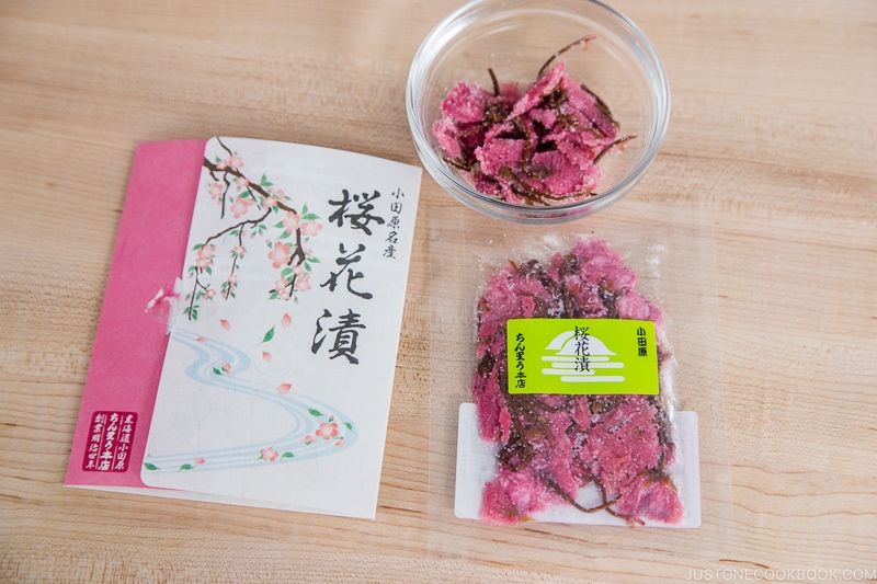 edible salt pickled cherry blossom in a glass bowl and package on top of cutting board