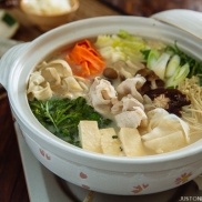 Japanese earthenware pot containing sliced pork belly, tofu, napa cabbage, carrot, leeks are cooking in a soy milk dashi broth.