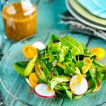 spring mix salad featuring avocado, heirloom tomatoes, radishes on a plate