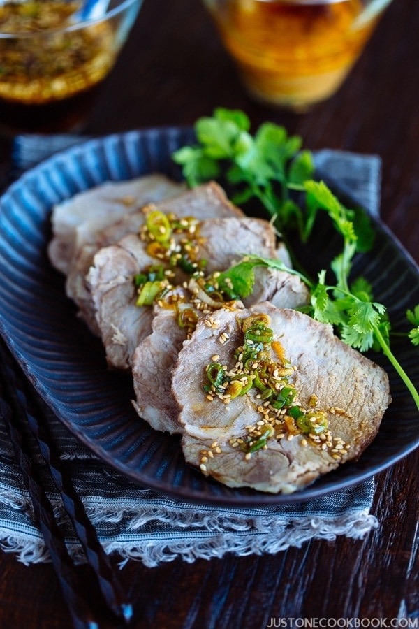 A dark plate containing sliced Pressure Cooker Steamed Pork topped with garlic soy sauce and garnished with cilantro.