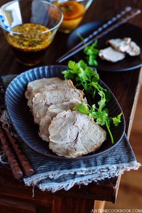Pressure cooker steamed pork thinly sliced and plated on a black dish accompanied by the two Asian dipping sauces.